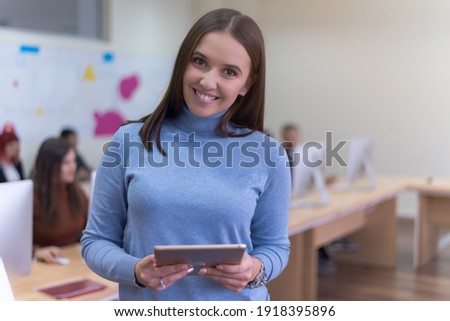 Portrait of a pretty cheerful casual turkish girl holding tablet or ipad inside modern computerlab classroom. Technology and education concept