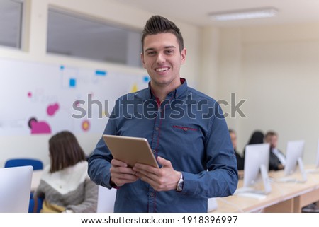 Portrait of casual turkish male student holding tablet or ipad inside modern computerlab classroom. Technology and education concept