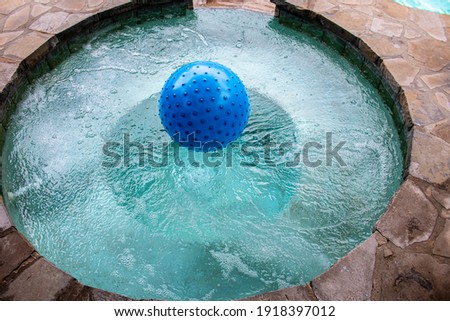 Bumpy blue beach ball floating in built-in hot tub in rock patio - top view