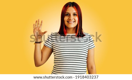 latin woman making goodbye or hello sign with red hair, on yellow background