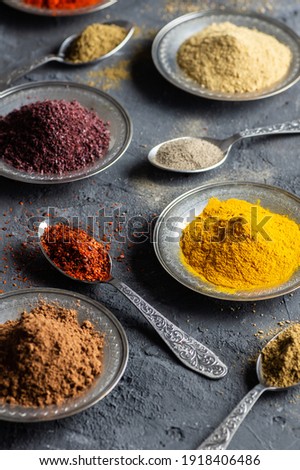 Assortment of natural spices on a vintage silver spoons or dishes on dark rustic stone background, Healthy spice concept