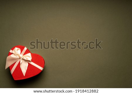 Red gift box heart shape with white ribbon on a green background, gift concept Valentine day, top view, copy space. High quality photo