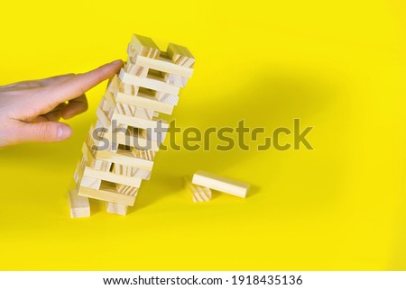 Wooden board game on a yellow background. People play a game of chance in which balance is important. The wooden block tower leans heavily and is about to collapse. Free space for text