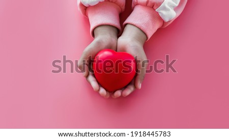 Little girl holding red heart in hand on pink background.