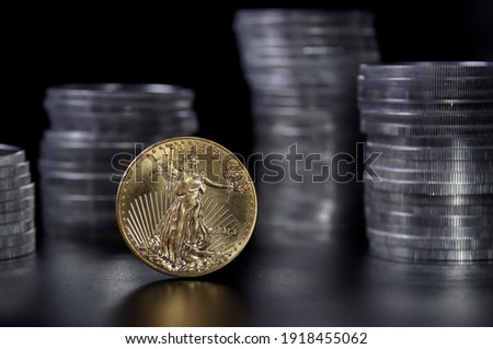 A one ounce gold coin in front stacks of 1 ounce American silver Eagle coins