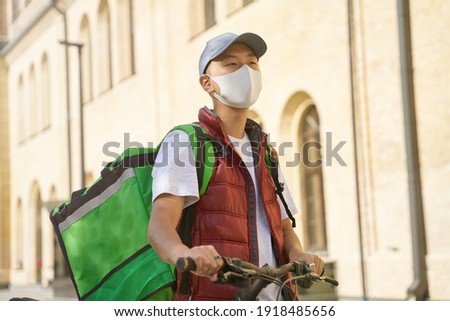 Young asian male courier with thermo bag wearing face protective
