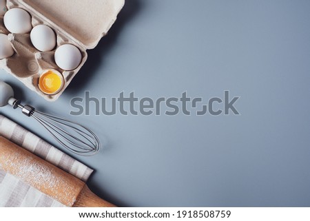 Different ingredients and kitchen utensils for making cookies or cupcakes, flat lay, copyspace. Eggs, rolling pin, whisk, flour, cookie molds, layout on a gray background. The concept of home baking.