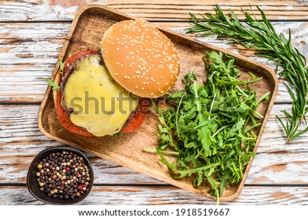 Big cheeseburger with beef, tomato, cheese and arugula. wooden background. Top view