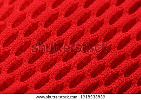 Fragment of a perforated toe of a red sneaker in full-screen close-up. Texture of the texture of the material of sports shoes.