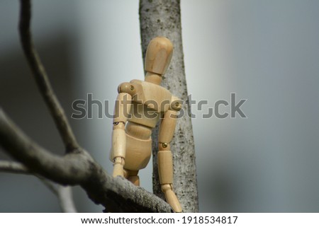 A wooden mannequin climbing on the branch of a tree