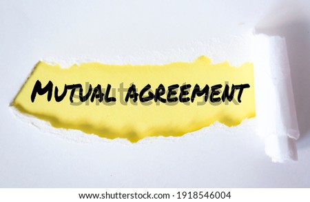 Torn white paper on yellow surface with "mutual agreement" word.