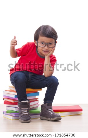Cute boy sitting on books and showing thumb up sign.