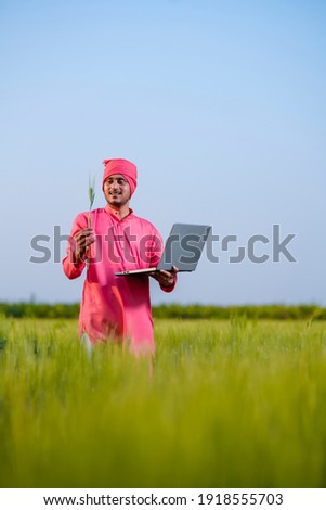 Young indian farmer using laptop at green wheat field