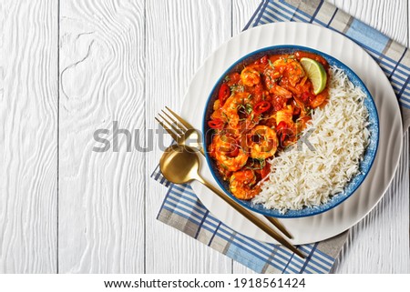 Tomato prawn curry of shrimps, chopped tomatoes with coriander sprouts and red chili on top served on a bowl with jasmine rice on white wooden background cutlery, top view, copy space, close-up Royalty-Free Stock Photo #1918561424