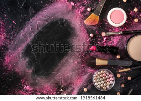 Make-up frame, formed by makeup products and tools and crushed cosmetics, overhead flat lay shot on black