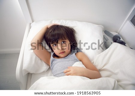 child boy lies in a white children's bed with a blanket in a room with toys rabbits