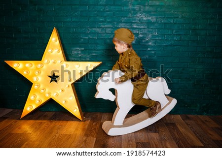 Portrait of little boy riding a horse. Children play with toys. The boy is preparing to learn pony riding. Hippotherapy for the development of the baby. Child in a suit. Kid riding white horse.