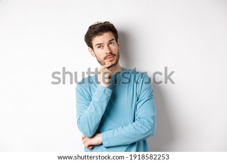 Image of handsome young man making choice, thinking and looking pensive up, standing over white background Royalty-Free Stock Photo #1918582253