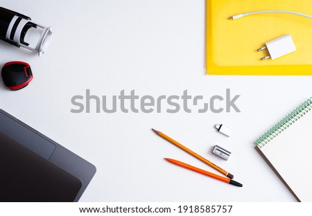Desktop. Stationery and laptop and mobile phone charger on white background. Gray and yellow. Panton colors 2021.