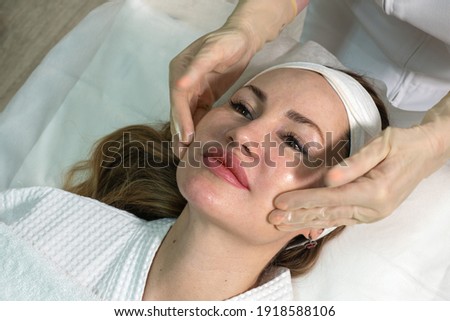 A young beautiful woman with open eyes gets a massage of the middle part of the face at the beauty institute. Close-up. Cosmetology. Procedure for a living. SPA treatment. Beauty salon. Beauty therapy Royalty-Free Stock Photo #1918588106