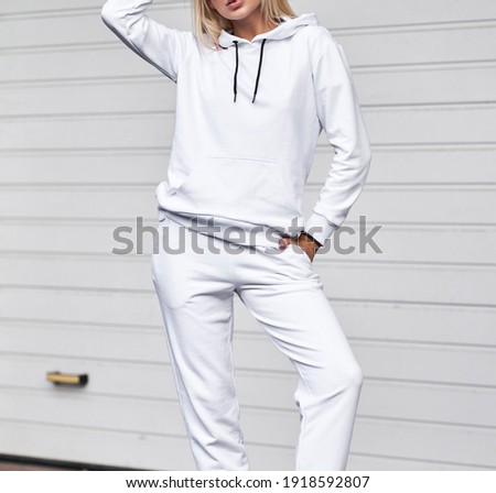 Woman is standing in white suit. Stylish streetwear without logos or pictures on blonde girl.