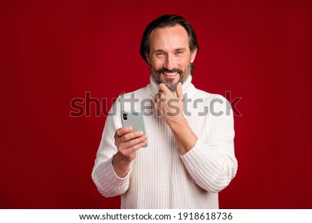 Photo of mature happy positive good mood cheerful man thinking using smartphone isolated on red color background