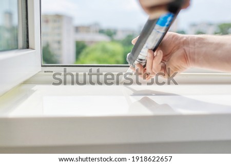 Artificial stone window sill, installation, technological process. Repair, construction of house, apartment. Worker with construction syringe fills seam between sill and window with silicone sealant Royalty-Free Stock Photo #1918622657