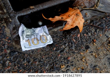 Money. American one hundred dollar bill on the edge of a storm drains grate after rain. Wet banknote and fallen yellow leaf on the metal grate. Close-up. Selective focus.