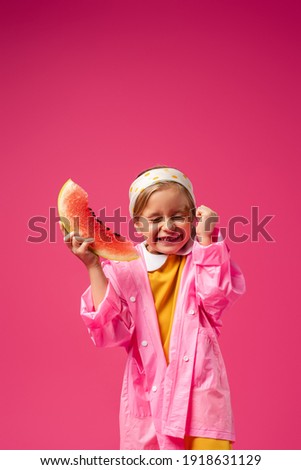 excited girl in raincoat holding watermelon on crimson