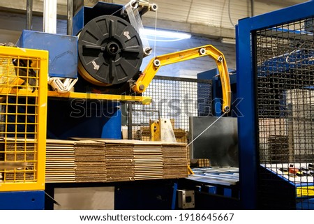 Ready-made cardboard boxes are moved in stacks along an automated packaging line. The strapping machine packs the stacks with thick white thread. Paper corrugated box factory. Royalty-Free Stock Photo #1918645667