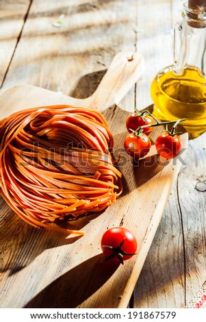 Ingredients for a tasty Italian tomato pasta dish with flavored linguine pasta. cherry tomatoes and olive oil on a chopping board on a rustoc wooden kitchen table
