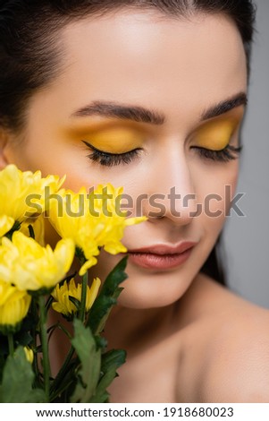 young woman with makeup and closed eyes near blooming yellow flowers isolated on grey