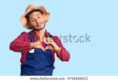 Handsome latin american young man weaing handyman uniform smiling in love doing heart symbol shape with hands. romantic concept. 