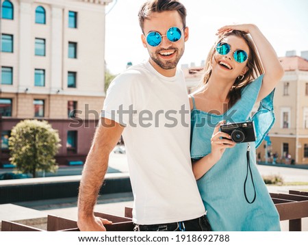 Portrait of smiling beautiful woman and her handsome boyfriend. Woman in casual summer jeans dress. Happy cheerful family.Female having fun. Couple posing on the street background with camera in hands