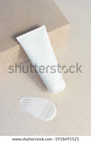 
white cosmetic tube for cream, body lotion, face cleanser or hand cream leaning against a suede box on a beige sandy background with a smear of cream. Delicate moisturizer concept, vertical Royalty-Free Stock Photo #1918695521