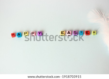 Happy Easter lettering text made of multicolored wooden letters and white feather on a soft blue background. Minimalistic holiday background.