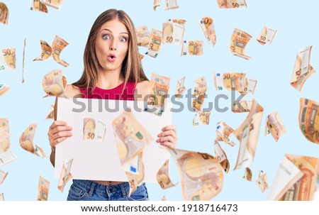 Young beautiful blonde woman holding blank empty banner scared and amazed with open mouth for surprise, disbelief face