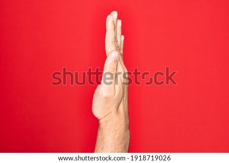 Hand of caucasian young man showing fingers over isolated red background showing the side of stretched hand, pushing and doing stop gesture