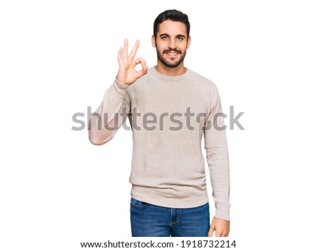 Young hispanic man wearing casual clothes smiling positive doing ok sign with hand and fingers. successful expression. 