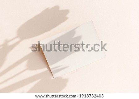 Blank card mockup on light pastel background with moody tulip flowers shadows and copy space, close-up top view.