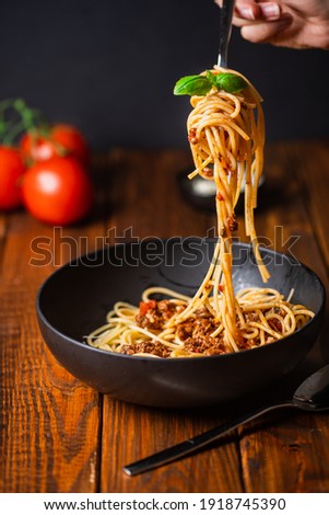 A hand holding a fork with spaghetti with bolognese tomato sauce in black bowl on wooden table Royalty-Free Stock Photo #1918745390