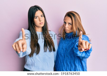 Hispanic family of mother and daughter wearing wool winter sweater pointing with finger up and angry expression, showing no gesture 