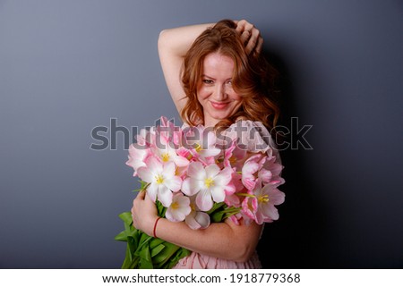 a young woman holds a bouquet of pink tulips on a gray background