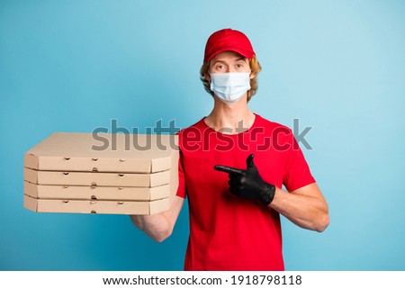 Portrait of delivery man direct finger pizzas wear hat t-shirt cold safety respiratory isolated on blue color background