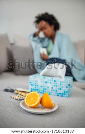 Medical care concept. Flu season. Sick woman covered with a blanket lying in bed with high fever and a flu, resting. Teapot, pills and lemon on the sofa, focus on the lemon and a teapot