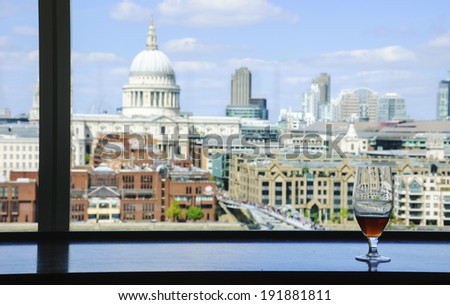 A glass of beer and a view from Tate Modern gallery's cafe on St Paul Cathedral with Millennium Bridge over Thames river. London, England. Reflections.