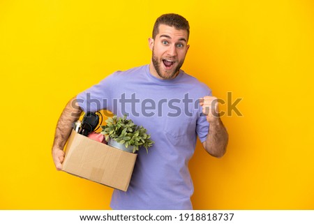 Young caucasian making a move while picking up a box full of things isolated on yellow background celebrating a victory in winner position