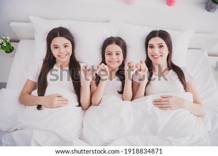 Photo of adorable sweet three siblings nightwear lying bed relaxing holding hands arms indoors inside room home