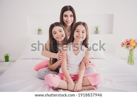 Photo of charming funny three sisters sleepwear sitting bed having rest smiling inside indoors home room