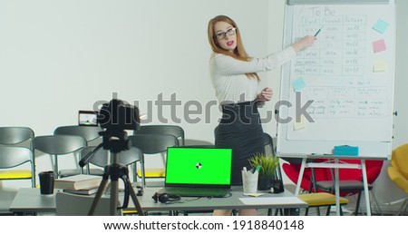 A woman is conducting an e-lesson from an empty classroom. Remote education, online education, remote studying, online learning concept. Green Screen Chroma Key Laptop for Learning.